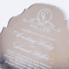 A silver mirror acrylic wedding invitation with a classic, ornate scalloped silhouette is shown at an angle against a white background. The highly reflective surface creates a liquid-like sheen, making the white printed text pop.