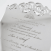 A luxurious silver mirror acrylic wedding invitation with a distinctive curved, shield-like silhouette. The top and bottom edges feature intricate laser-cut scrollwork that creates a decorative, open-work lace effect.