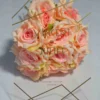 A transparent acrylic wedding invitation stands upright against a bouquet of peach-colored roses on a white surface. The invitation features elegant gold lettering and minimalist geometric gold lines in the corners.
