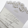 A luxurious silver mirror acrylic wedding invitation with a distinctive curved, shield-like silhouette. The top and bottom edges feature intricate laser-cut scrollwork that creates a decorative, open-work lace effect.