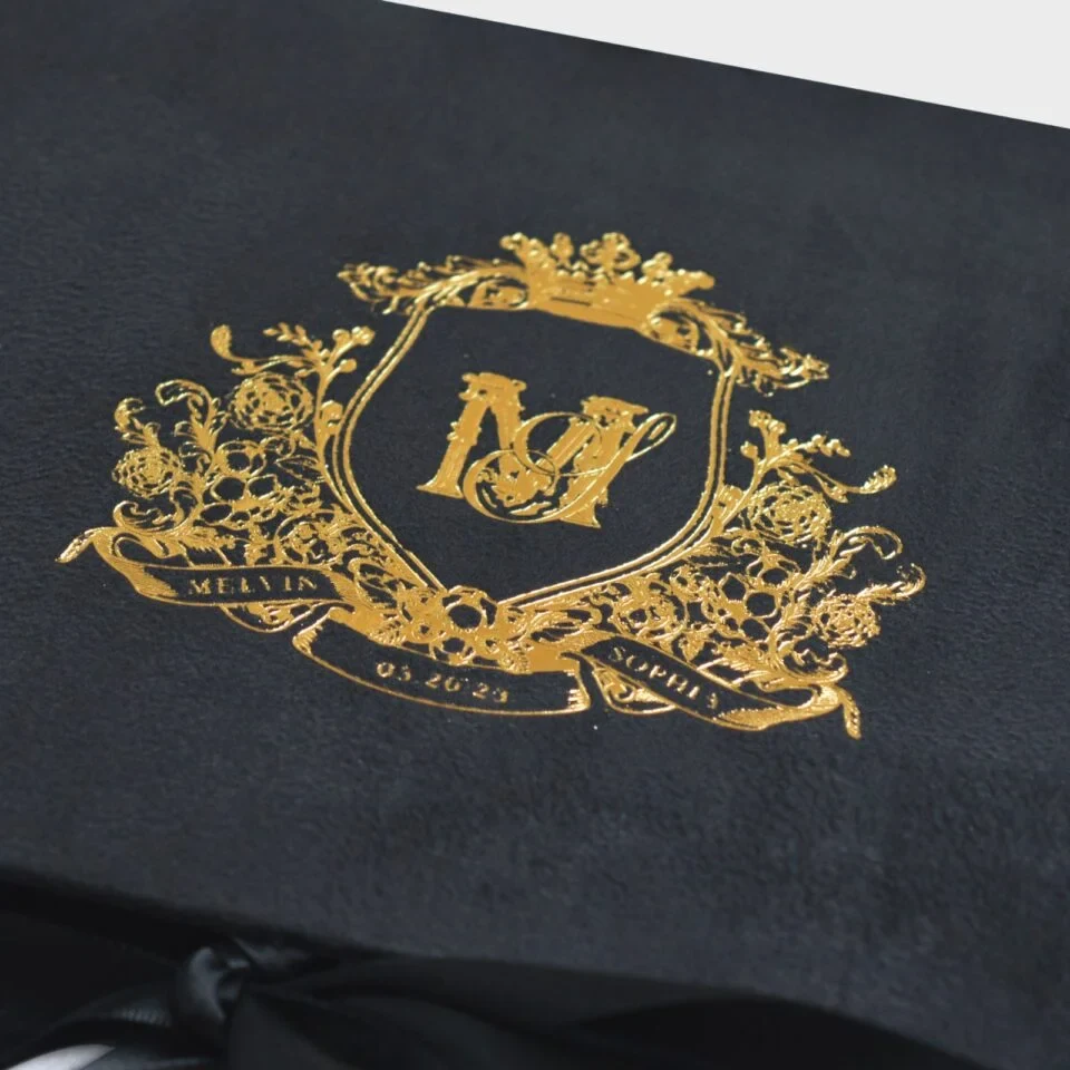 A high-angle view of an open **white luxury wedding invitation box** and its coordinating stationery. The inside lid features a gold-etched architectural illustration of a grand historic building. The suite includes: * A **clear acrylic invitation** with gold-foiled text and an intricate gold border, resting in a recessed compartment. * A **large ivory silk tassel** draped over the acrylic card. * An **RSVP card** with gold floral scrollwork in the corners. * An **Accommodations card** featuring elegant gold typography. * A white scalloped-edge envelope with a **gold foil monogram** on the flap. * Flowing **ivory satin ribbons** that weave through the arrangement on a clean white background.