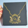 A top-down view of a **matte black square envelope** featuring a distinctively curved flap outlined with a thin **gold metallic border**. The envelope is secured by a large, ornate **gold crest seal** in the center, which showcases the monogram above the date in a matching metallic finish. To the left, a partial view of a **peach rose bouquet** provides a soft pop of color against the dark, formal stationery.