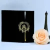 A graduation invitation presented in a luxurious black velvet gatefold folio. The folio is held closed by a black ribbon band featuring a gold ornate crest with an monogram. Inside, the invitation is printed on cream-colored cardstock with gold foil lettering.