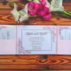 An open pale blush pink tri-fold wedding invitation suite laid flat on a rustic wood-grain surface, topped with a bouquet of vibrant pink and white gladiolus flowers. Center Panel: The main invitation card is white with a thin pink border and delicate pink floral illustrations in the corners. It features the name.the card is held in place by diagonal pink ribbons. Left and Right Panels: Each side features a blush pink pocket. The left pocket holds a details card, and the right pocket holds an RSVP card, both matching the floral theme and pink-on-white color scheme.