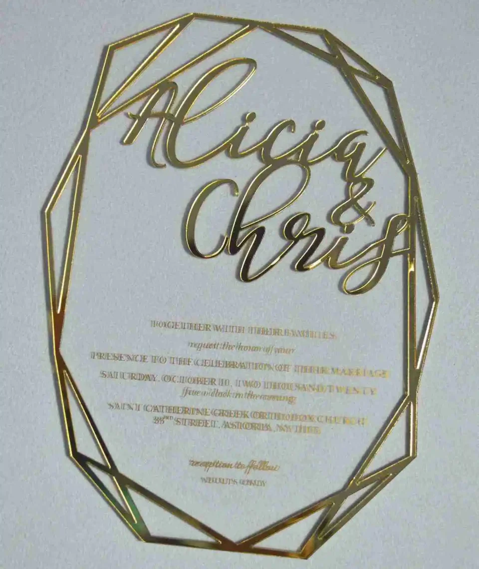 A transparent acrylic wedding invitation with a striking laser-cut geometric gold border. The invitation is hexagonal in its overall silhouette, featuring sharp, intersecting gold lines that create a crystalline frame.