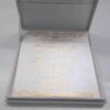 An open, **luxurious white wedding invitation box** featuring a formal stationery suite with gold accents. The interior includes: * A **white invitation card** in the base, printed with elegant **gold foil calligraphy** and framed by intricate gold scrollwork flourishes at the top and bottom. * The **inner lid** features a horizontal pocket holding a matching white card, also featuring a gold script heading. * The box is lined with a smooth, white fabric that gives it a clean and high-end appearance. * The top edge of the lid shows a hint of the **gold pearl-encrusted exterior**. * Set against a neutral, light grey background, the focus remains on the bright white textures and reflective gold detailing of the suite.