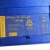 A high-angle view of a travel-themed wedding invitation set resting on a grey surface, featuring a royal blue silk passport invitation and a clear acrylic boarding pass. The suite includes:The Passport:Crafted from shimmering blue silk, it features the word "PASSPORT" and a large, intricate gold-foiled crest at the center. The names "**Rannice and Alphaus" and the date are printed at the bottom in elegant gold script.The Boarding Pass: A clear acrylic card designed to look like a flight ticket for "**All Eyez On Arrington Airways**." It features gold-etched details, including a barcode and the destination Decorative Accents: A cluster of soft peach-colored roses is placed in the background, adding a romantic contrast to the bold blue and gold stationery. The combination of luxury materials and a creative travel theme results in a unique and sophisticated invitation presentation.