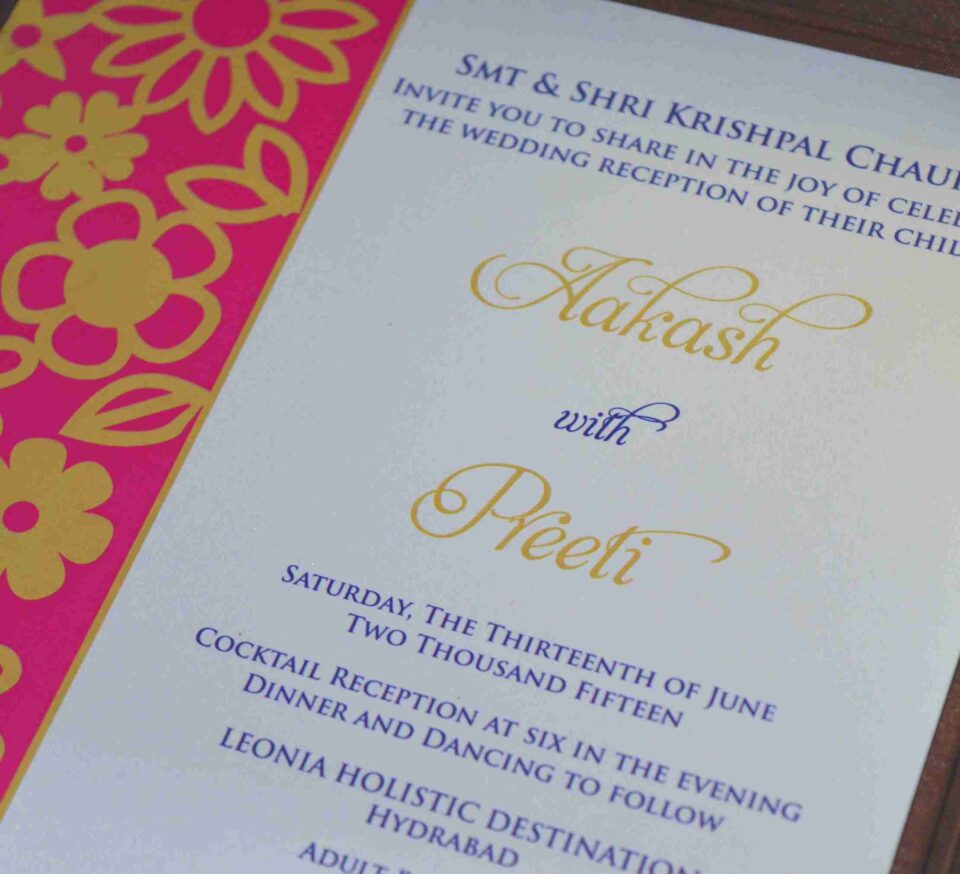 An open, chocolate-brown fabric invitation box displaying a formal wedding reception card. The card features a vibrant magenta left border with a gold laser-cut floral pattern. The main white section of the card includes elegant gold and purple typography for the names "Aakash with Preeti" and details for an event held in Hyderabad. The lid of the box is propped open, showing a matching design inside.
