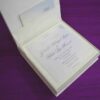 Here is the ALT text for the final image in your collection: **DSC_0293_165_11zon-960x804.jpg** An open, square ivory-colored wedding invitation box resting on a textured purple fabric surface. The interior lid features a horizontal pocket containing a small card for "Gabriella and Andre." The base of the box holds the main wedding invitation for "Gabriella Milagros Levin and Andre Leon Keavera," printed in elegant script on a white card with delicate corner flourishes.