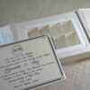 A flat-lay of a white wedding gift suite. It features a closed box with a crystal brooch, an open box base containing nine gold-wrapped chocolate truffles in a grid, a formal invitation for Mathew and Michelle, an RSVP card, and an envelope, all accented by pink flowers.