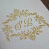 A high-angle, close-up shot of a **luxurious invitation box** with an ornate, three-dimensional lid design. The box features: * A **laser-cut gold wooden frame** on the lid with intricate floral and scrollwork patterns. * A central ** plaque** with a custom gold-etched monogram "R & F" in an elegant script. * A border of **sparkling clear crystals** embedded along the inner edge of the gold frame, adding a high-shine detail. * The rich, deep red velvet fabric covers the sides of the box, providing a soft, tactile contrast to the metallic gold top. * The box is displayed on a neutral, textured light-colored surface, highlighting its sophisticated and artisanal craftsmanship.