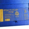 A high-angle view of a travel-themed wedding invitation set resting on a grey surface, featuring a royal blue silk passport invitation and a clear acrylic boarding pass. The suite includes:The Passport:Crafted from shimmering blue silk, it features the word "PASSPORT" and a large, intricate gold-foiled crest at the center. The names "**Rannice and Alphaus" and the date are printed at the bottom in elegant gold script.The Boarding Pass: A clear acrylic card designed to look like a flight ticket for "**All Eyez On Arrington Airways**." It features gold-etched details, including a barcode and the destination Decorative Accents: A cluster of soft peach-colored roses is placed in the background, adding a romantic contrast to the bold blue and gold stationery. The combination of luxury materials and a creative travel theme results in a unique and sophisticated invitation presentation.