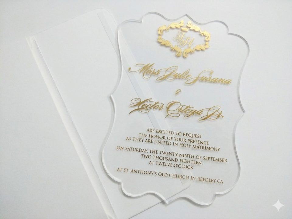 A transparent acrylic wedding invitation is shown partially tucked into a white paper pocket or sleeve. The image is shot at an angle on a white surface, highlighting the clarity of the invitation and the clean, minimalist presentation.
