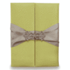 A rectangular, olive-green silk wedding invitation folio oriented vertically. The design features a gate-fold opening with two panels meeting in the center. A shimmering taupe or champagne-colored satin ribbon wraps horizontally around the folio, cinched at the middle by a large, sparkling silver rhinestone brooch with a geometric, butterfly-inspired silhouette. The folio is set against a plain white background, casting a soft shadow at the base.