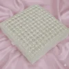 A high-angle, square shot of a **luxurious ivory-colored invitation box** resting on a draped, shimmering **pink satin fabric**. The design features: * A lid completely encrusted with a **geometric pattern of faux pearls**, arranged in precise rows and clusters. * Small **sparkling crystals** interspersed between the pearls, creating a quilted, high-shine effect. * The edges of the lid are bordered with smaller, uniform pearls for a clean finish. * The box sits at a slight angle, showcasing the smooth ivory sides and a small satin pull-tab. * The soft folds of the pink satin background provide a romantic, opulent texture that highlights the box's intricate details.