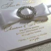 Ivory silk save the date card, adorned with a stunning rhinestone brooch on satin ribbon and printed with gold foil.
