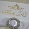Ivory silk save the date card, adorned with a stunning rhinestone brooch on satin ribbon and printed with gold foil.