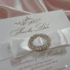 Ivory silk save the date card, adorned with a stunning rhinestone brooch on satin ribbon and printed with gold foil.