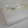 Ivory silk wedding invitation box with a luxury pearl brooch, satin ribbon, and handmade artisan padding.