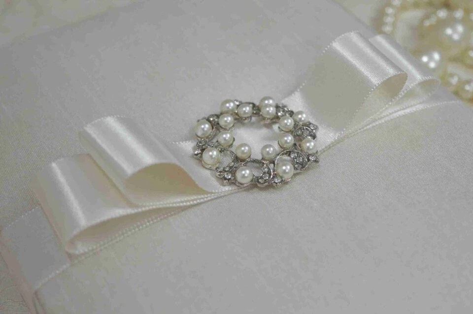Ivory silk wedding invitation box with a luxury pearl brooch, satin ribbon, and handmade artisan padding.