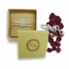 A top-down view of a square, gold silk invitation folio isolated against a white background. A matching gold satin ribbon is wrapped horizontally across the center, cinched by a large, circular brooch featuring white pearls and small, sparkling rhinestones. The fabric has a subtle, elegant sheen.