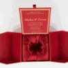 An overhead view of the open, deep red invitation box from the previous image. The two side flaps are spread wide, showing their angled, geometric construction. Inside the central compartment, a matching red card is framed by a double gold border. The card features the word "Venus" in elegant gold script, with a smaller line of gold text above it that reads, "Because there's no diamond too big or party too grand for." A small red ribbon pull-tab is visible at the bottom center of the box.