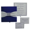 A top-down arrangement of a navy blue wedding stationery set. It includes a closed silk box featuring a wide white satin ribbon and a square crystal buckle. Beside the box is a formal white wedding invitation for Oliver Edwards and Emily Luna, a matching RSVP card, and a white envelope.
