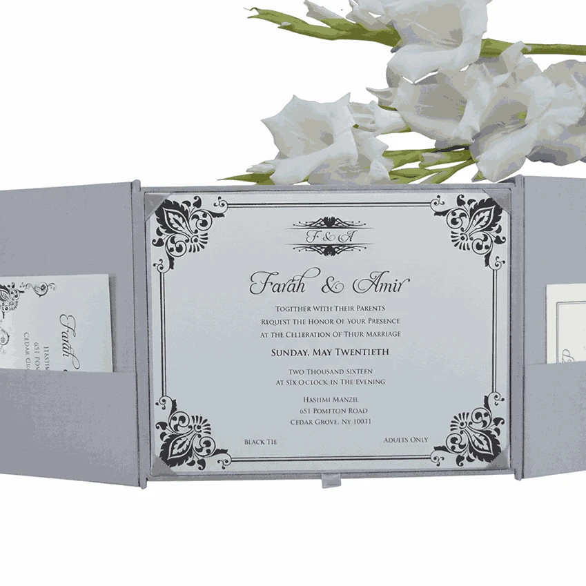 An open, light silver gatefold wedding invitation box displayed against a white background. The central panel features a white invitation card with elegant black script and intricate damask-style corner flourishes, announcing the marriage of Farah and Amir. The two side flaps have built-in pockets holding additional RSVP and detail cards. Above the box, a sprig of white gladiolus flowers with green buds provides a decorative accent.