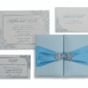 A square, light aqua-blue silk wedding invitation folio. The design features two gate-fold panels that meet in the center, wrapped horizontally with a wide, bright turquoise-blue satin ribbon. The ribbon is gathered at the center by a sparkling silver rhinestone brooch with a geometric, butterfly-like silhouette. The folio is set against a plain white background, casting a soft, subtle shadow.