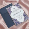 A white acrylic Bar Mitzvah invitation with an intricate Silver laser-cut Art Deco border is displayed on a shimmering dusty rose silk fabric. A small navy blue envelope sits behind it. The invitation features a Star of the top and the following details in gold script and serif fonts.