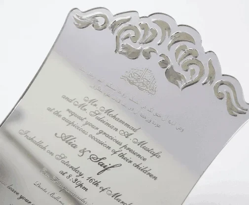A luxurious silver mirror acrylic wedding invitation with a distinctive curved, shield-like silhouette. The top and bottom edges feature intricate laser-cut scrollwork that creates a decorative, open-work lace effect.