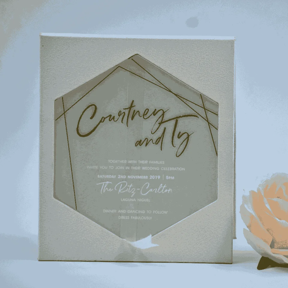 A modern and elegant cream-colored velvet wedding invitation box shown against a white background. The front of the box features a large hexagon-shaped cutout that serves as a window to the invitation inside.