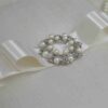 Ivory silk wedding invitation box with a luxury pearl brooch, satin ribbon, and handmade artisan padding.