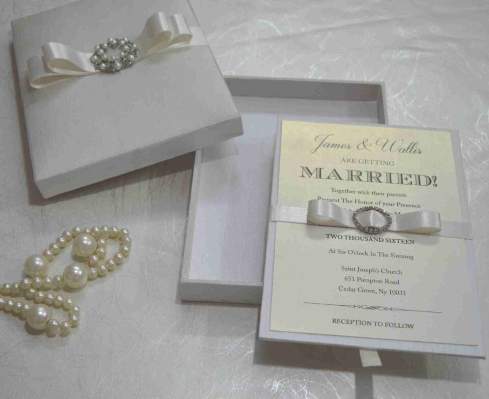 Handmade silk wedding invitation box adorned with a crystal rhinestone and pearl brooch for luxury wedding stationery.