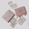 A top-down flat lay of a dusty rose wedding invitation suite on a grey background. The set includes a rose velvet rectangular box with a gold-foiled royal crest and the names tied with a matching pink satin bow.