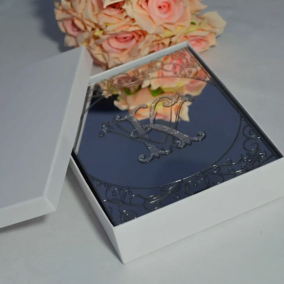 A high-angle shot of an open, champagne-colored silk wedding invitation Box featuring a large, ornate gold crystal-embellished brooch on the left panel. The suite includes: A clear acrylic wedding invitation with white script lettering for the name resting inside the folio. A coordinating ivory envelope with a gold-foiled return address on the flap.The arrangement is decorated with a peach-colored rose in the upper-right corner and a vintage gold lantern in the upper-left, all set against a clean white surface.