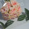 A close-up, angled shot of a clear acrylic Bat Mitzvah invitation resting against a bouquet of peach-colored roses and green leaves . The transparency of the acrylic allows the soft petals of the roses to be seen through the card.