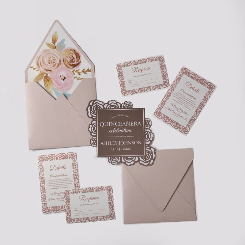 An elegant Quinceañera invitation suite featuring a dusty rose and rose gold color palette, laid out on a light gray background. The set includes several coordinated pieces: Main Invitation: A square, chocolate-brown card with a decorative rose gold laser-cut floral border made of rose patterns. The white and rose gold text reads, "PLEASE JOIN US FOR A QUINCEAÑERA celebration IN HONOR OF ASHLEY JOHNSON" with the date "11.24.2024." Enclosure Cards: Three white cards featuring a matching rose gold floral pattern around the edges. These include two "Response" (RSVP) cards and one "Details" card for accommodations. Envelope: A dusty rose envelope is shown open, revealing a luxurious floral liner featuring large painted roses in shades of cream, pink, and gold with gold leaf accents. A second invitation card is partially tucked inside.