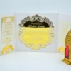 An open white wedding invitation folio featuring a striking gold mirror acrylic centerpiece. The centerpiece is die-cut into an ornate, scalloped shield shape with filigree borders, reflecting the names printed in white script.