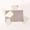 An open, mauve-colored velvet folio and Acrylic wedding invitation set displayed on a white background. The folio features a pocket on the left side holding a cream-colored envelope with a printed address, and a "Celebration" card with a silver border resting in front.