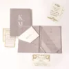 An open, mauve-colored velvet folio and Acrylic wedding invitation set displayed on a white background. The folio features a pocket on the left side holding a cream-colored envelope with a printed address, and a "Celebration" card with a silver border resting in front.