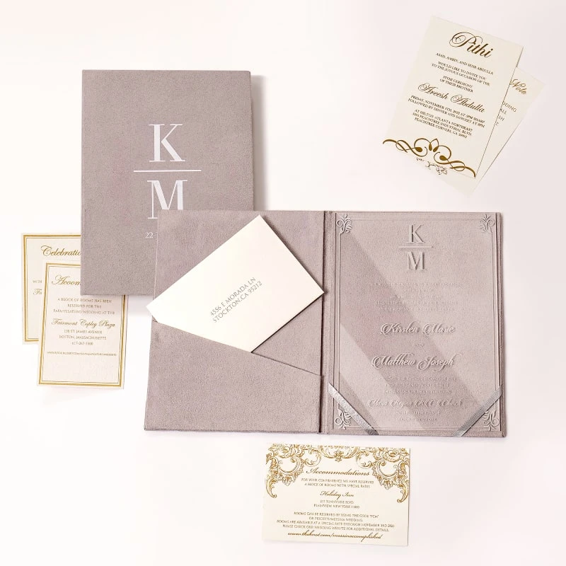 An open, mauve-colored velvet folio and Acrylic wedding invitation set displayed on a white background. The folio features a pocket on the left side holding a cream-colored envelope with a printed address, and a "Celebration" card with a silver border resting in front.