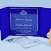 An open royal blue velvet tri-fold wedding invitation shown from a slightly elevated angle. The central panel holds a clear acrylic invitation card with crisp white text, featuring the names in an elegant script.