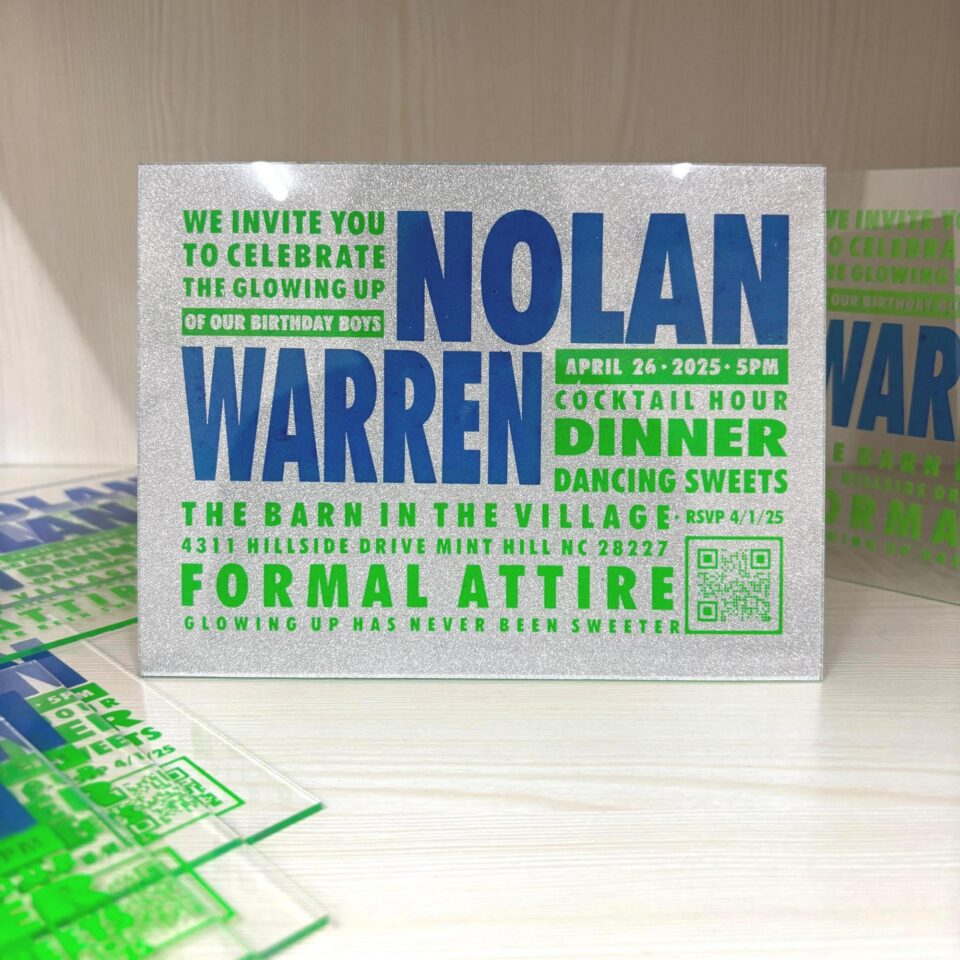 A vibrant, modern birthday invitation for printed on a shimmering silver glitter background. The design features a bold, blocky typography layout in alternating electric green and royal blue. The text invites guests to "Celebrate the Glowing Up" of the birthday boys and includes event details like dinner, dancing, and formal attire, alongside a QR code in the bottom right corner. Several other clear acrylic and glitter invitations are scattered on a light wood surface in the background.