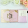 A high-angle view of an open pink silk gatefold invitation folio displayed on a white surface, accompanied by white and peach roses. The fairy-tale-themed suite includes: The center panel: Features a pink invitation card with a gold-bordered frame and the heading. It announces the celebration for in elegant gold script. Side pockets: The left and right panels contain pockets holding coordinating white cards with gold-foiled accents.Decorative details: Intricate gold laser-cut butterflies are tucked into the corners of the main invitation, which is secured by a thin pink satin ribbon pull-tab. The overall design is whimsical and romantic, using a soft pastel palette and shimmering gold highlights.