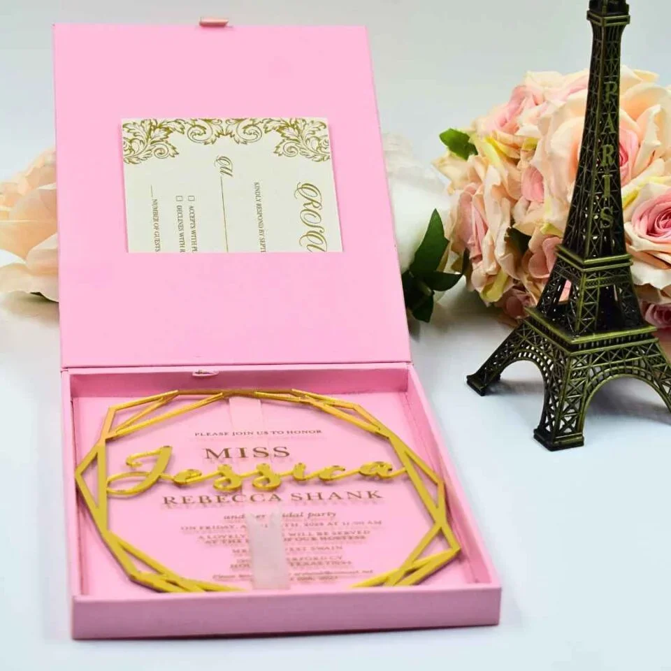 A high-angle view of a luxurious, open emerald velvet wedding invitation box displayed on a light surface. The stationery suite includes:Inside Lid: A gold-bordered card featuring an elegant gold-etched illustration of a historic, multi-story building with palm trees. The Base:A clear acrylic invitation card rests in a recessed compartment. It features the names and wedding details in a mix of white script and serif typography.Accessories: A thick emerald green silk tassel is attached to the invitation, and a matching green velvet band with a gold wax seal is visible in the base.Decor: A small bronze Eiffel Tower figurine stands to the right, and a soft peach-colored rose is positioned on the left, adding to the sophisticated travel-themed aesthetic.