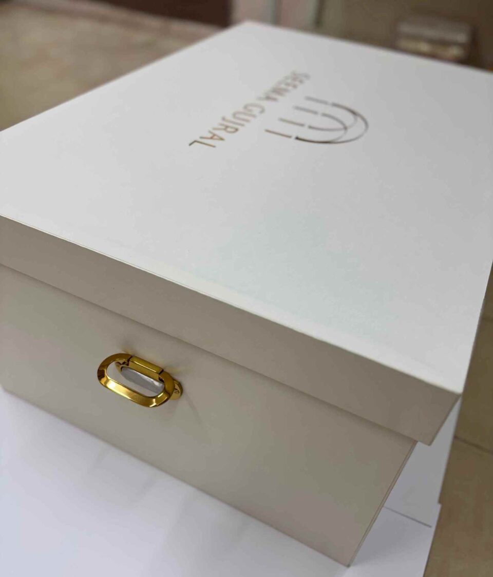 Luxury bridal lehenga box crafted from 7mm MDF featuring a white pearl shimmer finish, custom gold foil branding for a fashion designer, and premium side handles for couture trousseau packaging.