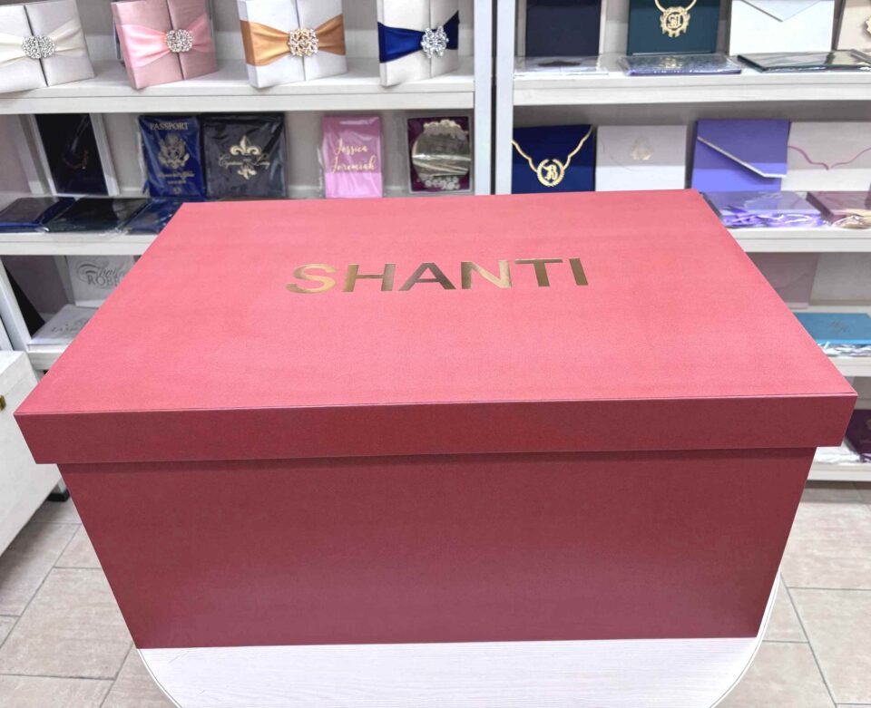 A high-end bridal lehenga trunk box made of a thick orange MDF frame with a smooth matte finish, featuring a custom gold foil-pressed logo on the lid and a sturdy antique brass handle on the side for professional fashion packaging.