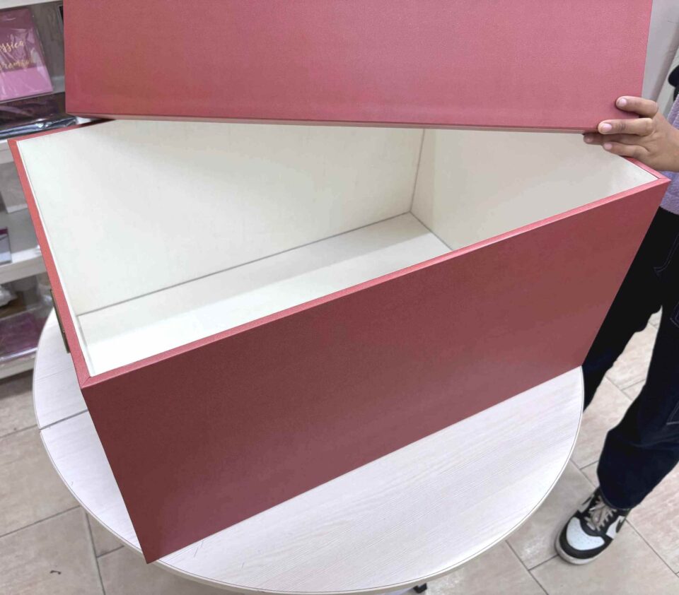 A high-end bridal lehenga trunk box made of a thick orange MDF frame with a smooth matte finish, featuring a custom gold foil-pressed logo on the lid and a sturdy antique brass handle on the side for professional fashion packaging.