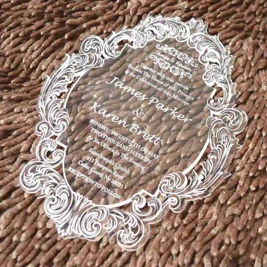 Clear acrylic wedding invitation with white engraved baroque frame, styled on a brown textured throw